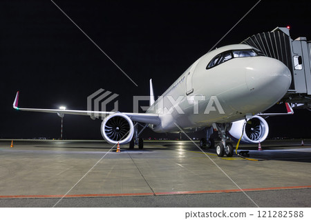 A white passenger jet plane stands at the air bridge connected to an external power supply on an airport night apron 121282588