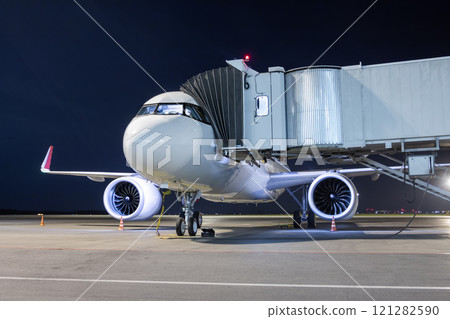 A white passenger jet plane at the air bridge connected to an external power supply on an airport night apron A white passenger jet plane at the air bridge connected to an external power supply on an airport night apron 121282590