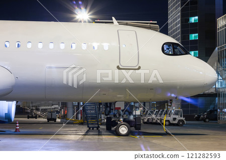 The front part of the white passenger jet plane on the airport apron near the air bridge and terminal at night The front part of the white passenger jet plane on the airport apron near the air bridge and terminal at night 121282593