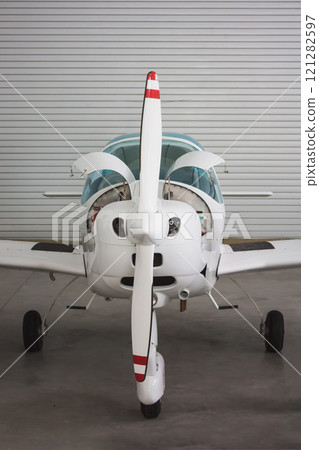 Close front view of a small white sports plane in a hangar. The aircraft has an open engine Close front view of a small white sports plane in a hangar. The aircraft has an open engine 121282597