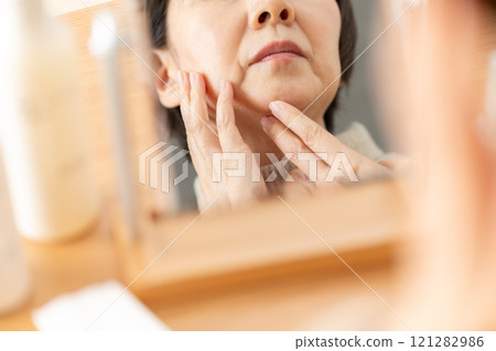 Middle-aged to senior women doing skin care while looking in the mirror Middle-aged to senior women doing skin care while looking in the mirror 121282986