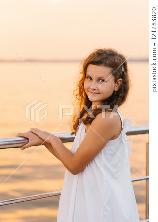 Child girl stands on pier by the water, wearing white dress. The scene is serene and peaceful, with the girl's smile reflecting the beauty of the moment Child girl stands on pier by the water, wearing white dress. The scene is serene and peaceful, with the girl's smile reflecting the beauty of the moment 121283820