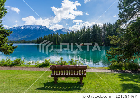 Jasper National Park summer landscape, Alberta, Canada. Wooden bench on lakeside of the Beauvert Lake (Lac Beauvert). Snowcapped Whistlers Peak mountain in the background. 121284467