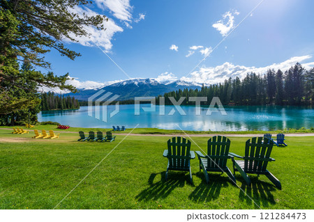 Jasper National Park summer landscape, Alberta, Canada. Adirondack chairs on lakeside of the Beauvert Lake (Lac Beauvert). Snowcapped Whistlers Peak mountain in the background. 121284473