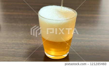將生啤酒倒入玻璃杯中，金黃的啤酒和溢出的氣泡 121285460