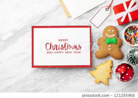 Merry christmas holiday card and red envelope with gingerbread cookie and christmas decor  on marble table 121285968