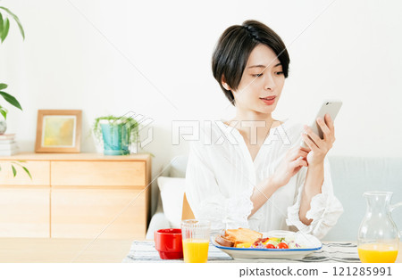 年輕女子一邊吃飯一邊看智慧型手機 121285991