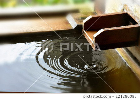 A drop of water and ripples from the spout of an open-air cypress bath 121286083