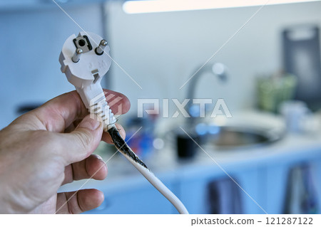 Burnt out cable with an electrical plug in hand of user who has overloaded an extension cord with tee. 121287122