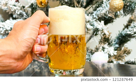 Male hand holding draft beer against the background of a Christmas tree 121287649