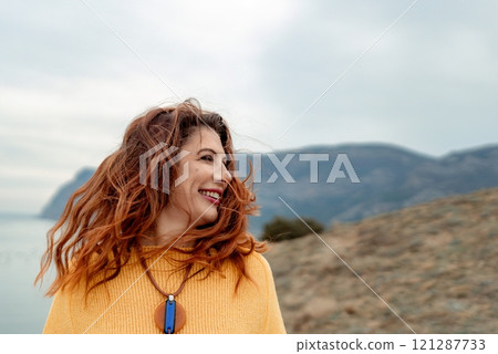 Portrait windswept hair happy woman against a backdrop of mountains and sea. Daylight illuminates the tranquil outdoor setting 121287733