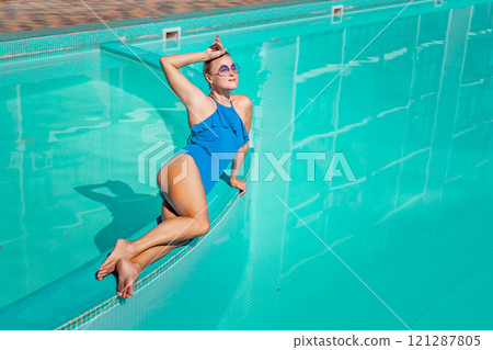 Bikini-clad woman enjoys poolside relaxation. Poolside ambiance. Capturing woman's relaxed time near pool. 121287805