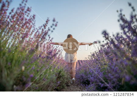 A woman is walking through a field of purple flowers with a straw hat on A woman is walking through a field of purple flowers with a straw hat on 121287834