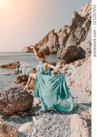 Woman green dress sea. Woman in a long mint dress posing on a beach with rocks on sunny day. Girl on the nature on blue sky background. 121287852