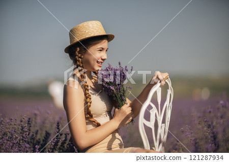 girl sitting field lavender and wearing a straw hat. She is smiling and holding a bouquet of flowers girl sitting field lavender and wearing a straw hat. She is smiling and holding a bouquet of flowers 121287934