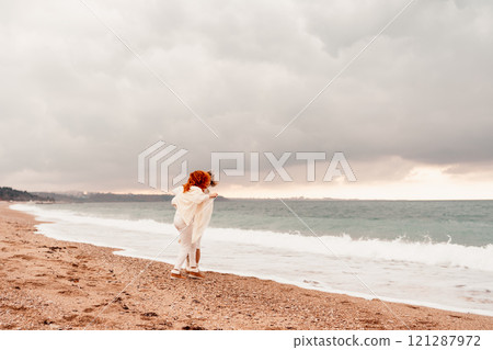 Women sea walk friendship spring. Two girlfriends, redhead and blonde, middle-aged walk along the sandy beach of the sea, dressed in white clothes. Against the backdrop of a cloudy sky and the winter Women sea walk friendship spring. Two girlfriends, redhead and blonde, middle-aged walk along the sandy beach of the sea, dressed in white clothes. Against the backdrop of a cloudy sky and the winter 121287972