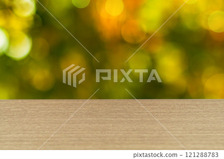 The surface of the table has a texture of light walnut, oak, hornbeam or other hardwoods, edge of table is defocused, on blurred early autumn orange-green background. Blank for design, copy space The surface of the table has a texture of light walnut, oak, hornbeam or other hardwoods, edge of table is defocused, on blurred early autumn orange-green background. Blank for design, copy space 121288783