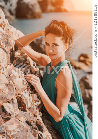Woman green dress sea. Woman in a long mint dress posing on a beach with rocks on sunny day. Girl on the nature on blue sky background. Woman green dress sea. Woman in a long mint dress posing on a beach with rocks on sunny day. Girl on the nature on blue sky background. 121289118