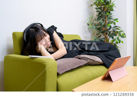 A young woman wearing headphones and watching videos on a tablet in the living room Watching videos Live broadcast Lying down A young woman wearing headphones and watching videos on a tablet in the living room Watching videos Live broadcast Lying down 121289338