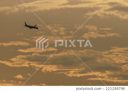 一架飛機起飛進入橘色的天空,這是出發的標誌。 一架飛機起飛進入橘色的天空,這是出發的標誌。 121289796