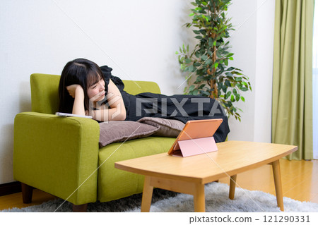 年輕女性在客廳的平板電腦上觀看影片、觀看影片、現場評論、躺著 年輕女性在客廳的平板電腦上觀看影片、觀看影片、現場評論、躺著 121290331