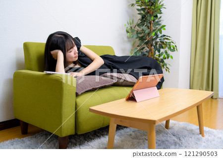 A young woman falls asleep while watching videos on a tablet in the living room. Falling asleep, watching videos, live broadcast, lying down 121290503