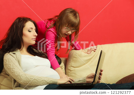 Pregnant woman and daughter sitting with laptop 121292377