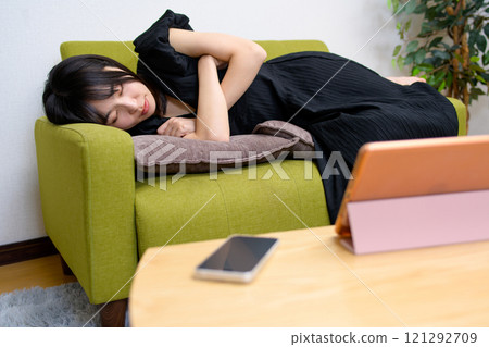 一位年輕女子在客廳的平板電腦上觀看影片時睡覺。 一位年輕女子在客廳的平板電腦上觀看影片時睡覺。 121292709
