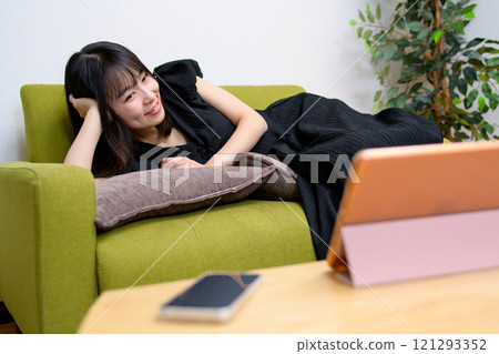 Young woman watching videos on a tablet in the living room, watching videos, live broadcast, lying down Young woman watching videos on a tablet in the living room, watching videos, live broadcast, lying down 121293352