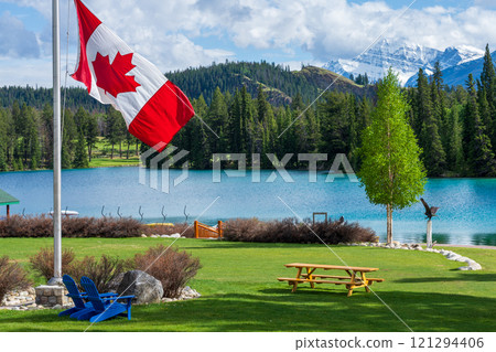 Canadian flag and mountains and trees. Jasper National Park summer landscape. Lac Beauvert Trail (Beauvert Lake). Canadian flag and mountains and trees. Jasper National Park summer landscape. Lac Beauvert Trail (Beauvert Lake). 121294406