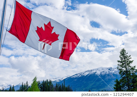 Close up of National Flag of Canada with trees and snow-capped mountains in the background. 121294407