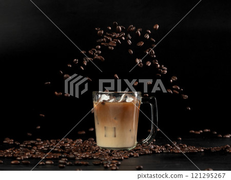 Ice Latte Coffee in glass with roasted bean falling. Black background isolated element. Many Coffee Beans fall on Ice milk cold drink with aroma scent Ice Latte Coffee in glass with roasted bean falling. Black background isolated element. Many Coffee Beans fall on Ice milk cold drink with aroma scent 121295267