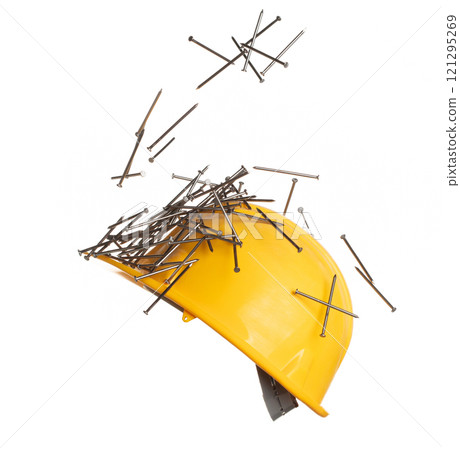 Construction supply equipment long nails fall into safety hard yellow hat as accident. Safety Hat protect supply long nails from accident falling hit head. White background isolated Construction supply equipment long nails fall into safety hard yellow hat as accident. Safety Hat protect supply long nails from accident falling hit head. White background isolated 121295269