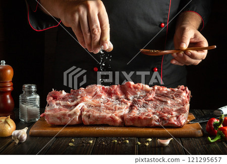 A skilled chef expertly sprinkles salt over a large piece of raw meat on a wooden cutting board A skilled chef expertly sprinkles salt over a large piece of raw meat on a wooden cutting board 121295657