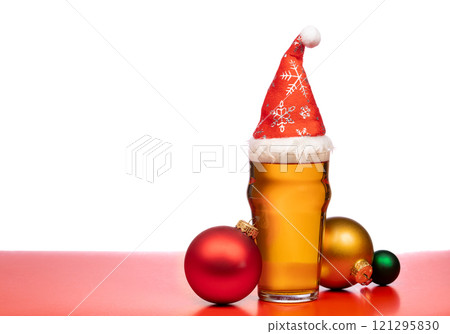 Festive beer glass with a Santa hat surrounded by colorful Christmas baubles on a red background 121295830