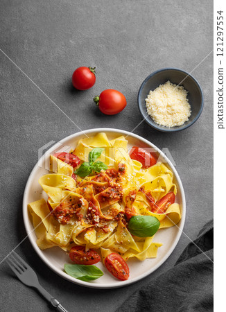 Tagliatelle pasta with tomato sauce, basil and parmesan cheese in a plate on a dark background. Tagliatelle pasta with tomato sauce, basil and parmesan cheese in a plate on a dark background. 121297554