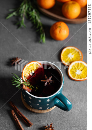 Mulled wine with orange, cinnamon and rosemary in a cup on a dark background with tangerines. Mulled wine with orange, cinnamon and rosemary in a cup on a dark background with tangerines. 121297558