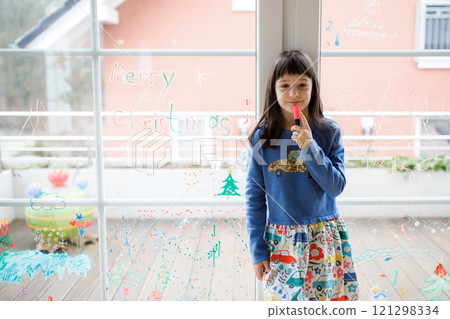 Smiling girl looking at christmas drawings on window Smiling girl looking at christmas drawings on window 121298334