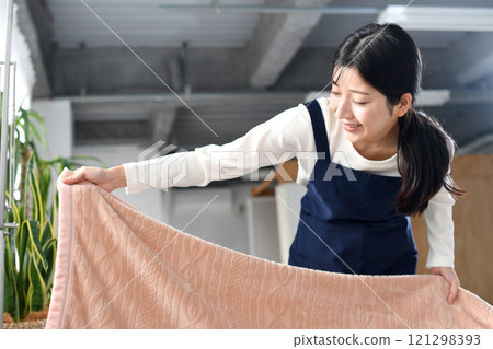 A woman in an apron making a bed 121298393