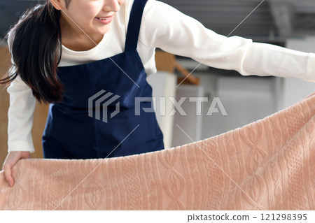 一個穿著圍裙的女人正在整理床鋪 121298395