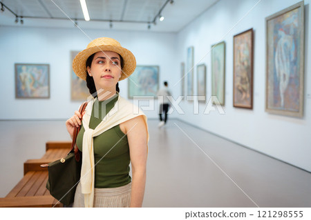 Mid shot of elegant young Caucasian woman in straw hat posing in the art gallery. Copy space. Concept of cultural education and Museum Day 121298555