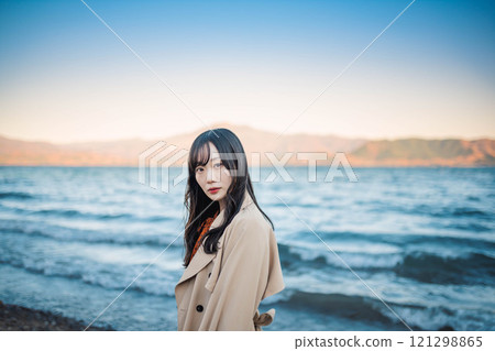 A young woman in a trench coat with blue sky and a lake 121298865