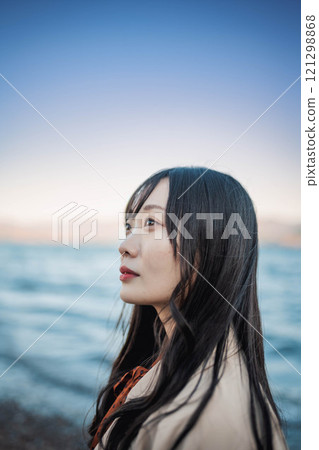 A young woman in a trench coat with blue sky and a lake 121298868