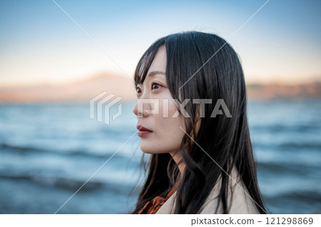 A young woman in a trench coat with blue sky and a lake 121298869