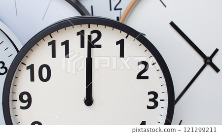 A collection of round wall clocks overlapping each other, with one clock prominently showing the time as 12 o'clock. Clean design with bold black numbers and hands on white dials. 121299211