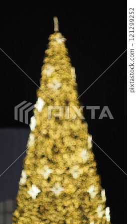 A stunning out-of-focus image capturing a glowing Christmas tree, adorned with warm golden lights and faint star-shaped highlights, set against a dark background. The bokeh effect creates a magical 121299252