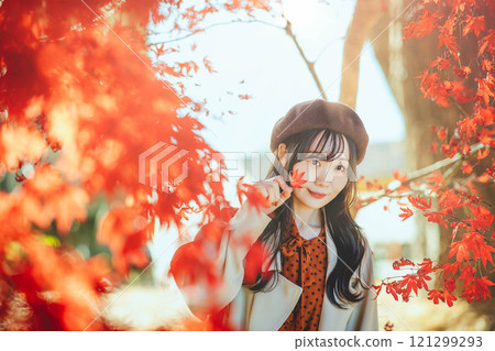 A young woman wearing a beret looking at autumn leaves 121299293