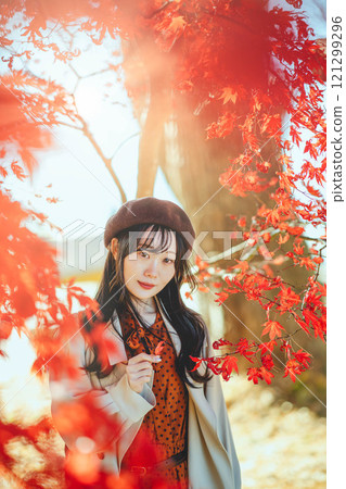 A young woman wearing a beret looking at autumn leaves 121299296
