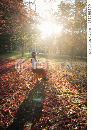 A young woman wearing a beret looking at autumn leaves 121299309