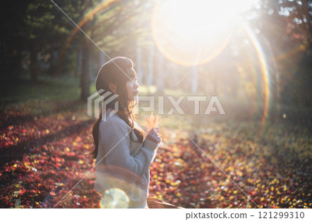 A young woman wearing a beret looking at autumn leaves 121299310